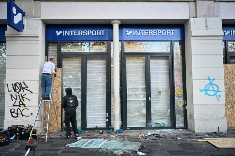 Des employés installent des panneaux en bois sur la vitrine brisée d'un magasin au landemain d'une manifestation contre la vie chère, le 18 octobre 2026 à Paris