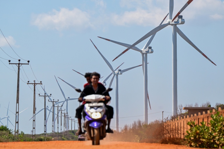 Cette photo, prise le 2 octobre 2026, montre un motard passant devant des éoliennes installées le long d'une route de la péninsule de Mannar, au Sri Lanka