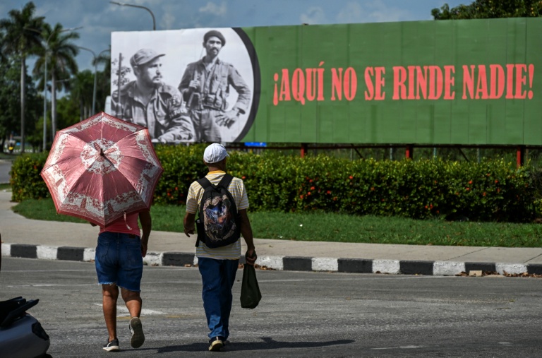 Des Cubains devant une affiche à l'effigie du défunt dirigeant cubain Fidel Castro (1926-2016) et du commandant Juan Almeida Bosque (1927-2009) sur laquelle est écrit 