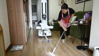 Un robot assistant ménager transporte une bouteille jusqu'à une poubelle tandis qu'une femme de ménage nettoie le sol chez une cliente à Pékin, le 21 mai 2026 en Chine