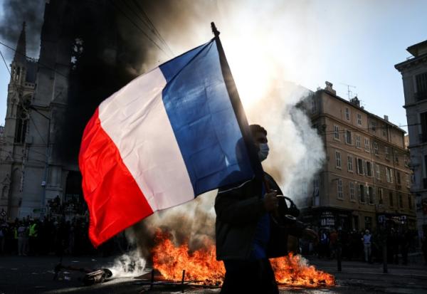 Un manifestant avec un drapeau français devant un feu, le 17 octobre 2026 à Marseille